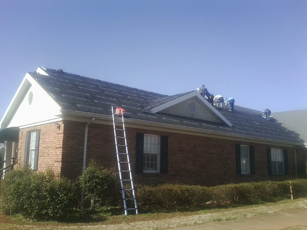 Crew tearing shingles off a brick ranch roof with a ladder set — Metal Roof Repair work by our crew in Wilkeson