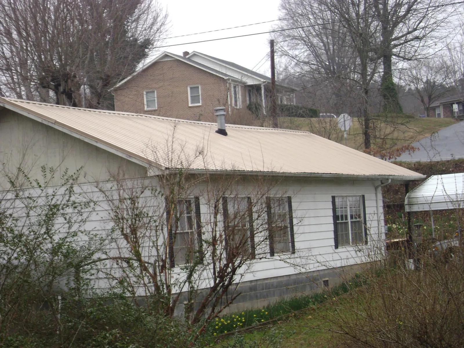 Tan metal roof on a white sided house set into a hillside — Commercial Roofing by Roofing Brothers in Wilkeson